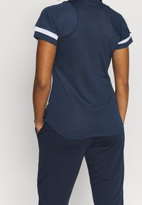 Navy urheilu t-paita, jossa on istuva malli, lyhyet hihat ja valkoiset korostourat. Valmistettu teksturoidusta, kosteutta siirtävästä kankaasta.