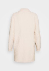 Light beige knit sweater with a high collar, featuring a diamond pattern and ribbed cuffs. Loose fit and long sleeves with subtle texture.