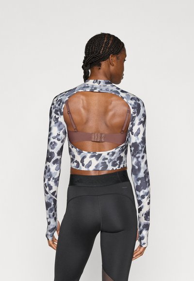 Αθλητικό τοπ μακρυμάνικο με σχέδιο λεοπάρ σε γκρι και μαύρο, ανοιχτή πλάτη, με καφέ αθλητικό σουτιέν από κάτω. Μαύρα κολάν.