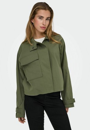 Giacca cropped di colore verde oliva, realizzata in tessuto morbido, con una grande tasca frontale, un design minimalista e maniche arrotolate.