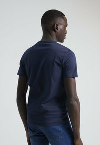 Camiseta de algodón de manga corta en azul marino con un escote redondo y textura suave, vista desde la parte posterior. Combínala con jeans azules visibles en la cintura.