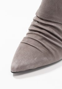 Pekig tå grå ankelstövlar i mjukt mocka, med veckat omslutande runt skaftet och en tunn svart sula.