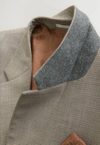 Blazer con tela a cuadros beige. Presenta un cuello de lana gris y un forro interior marrón con patrón, mostrando solapas estructuradas y detalle de bolsillo.