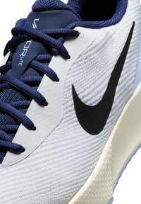 Nike tenisice u bijeloj boji s plavim detaljima, s teksturiranim gornjim dijelom, crnim swoosh logotipom i mornarsko plavim vezicama. Lagani dizajn s mekim đonom.