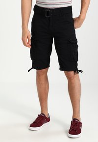 Pantaloni cargo neri con tasche e lacci laterali regolabili. Realizzati in tessuto resistente, dotati di cintura e vestibilità comoda. Abbinati a scarpe da tennis bordeaux.