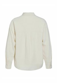 Camisa de manga larga color crema con un corte relajado, puños abotonados, un pliegue en la parte posterior y un collar, fabricada en un suave tejido texturizado.