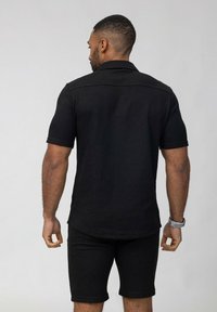 Polo noir à manches courtes, en tissu texturé, associé à un short noir. L'ensemble a une coupe moderne et un motif de design subtil.