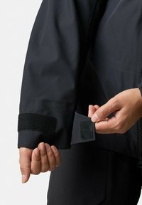 Czarna wodoodporna rękaw z regulowanym paskiem na rzep; gładka tekstura; ręka trzymająca klapę odsłaniającą dodatkowe ustawienie na rzep.