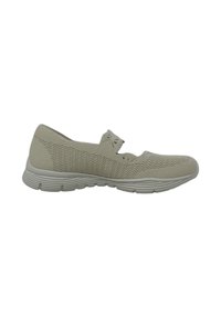 Zapatilla deportiva de color beige claro con parte superior de punto texturizado, punta redondeada y detalle de cinta elástica. Suela de goma con un patrón de relieve sutil.