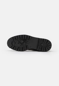 Black rubber sole of a shoe with deep treads and patterned grip, positioned horizontally on a plain white background.