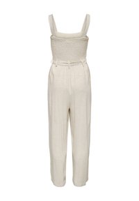 Combinaison beige sans manches avec corsage smocké, larges bretelles, ceinture à la taille et pantalon droit.