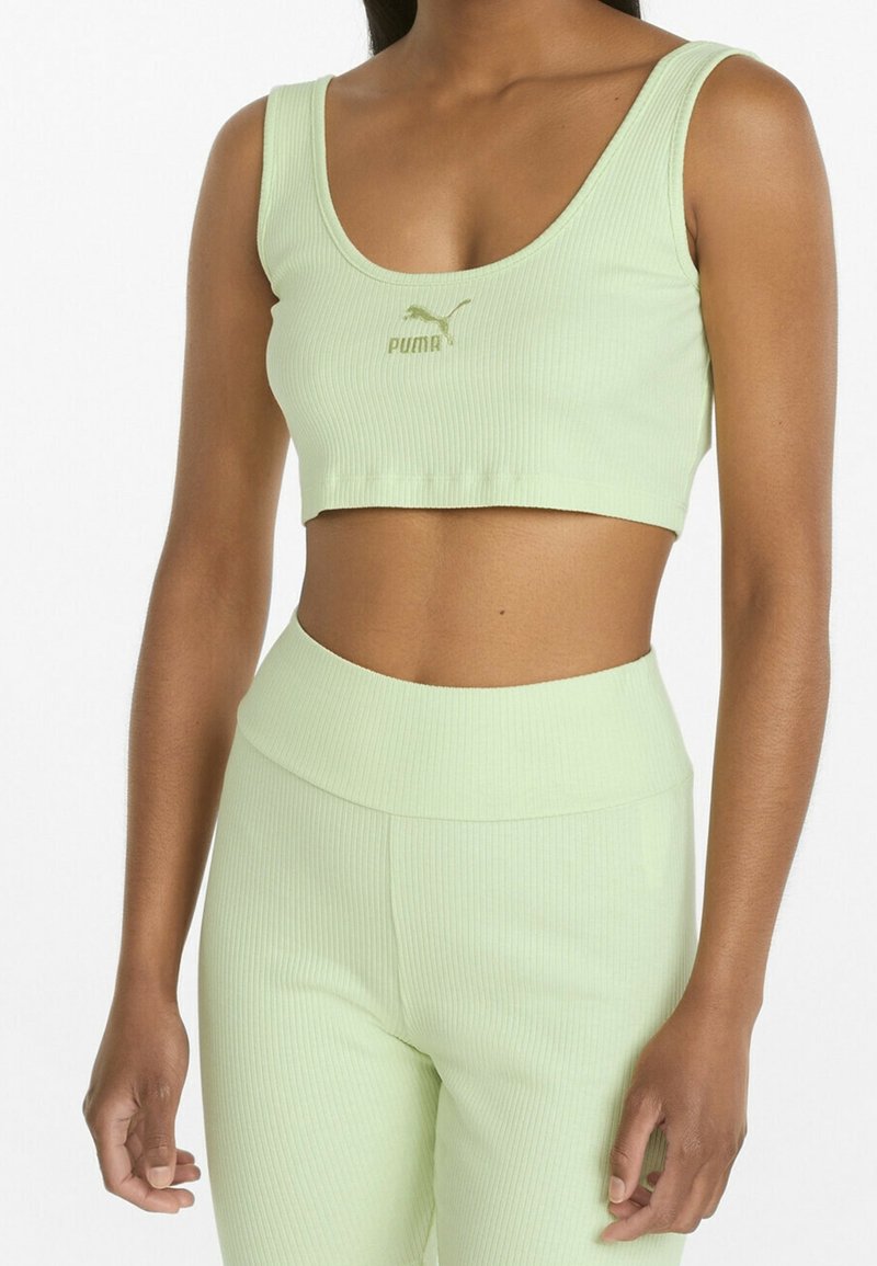 Femme portant un crop top côtelé vert clair et un legging taille haute assorti, affichant le logo Puma sur la poitrine.