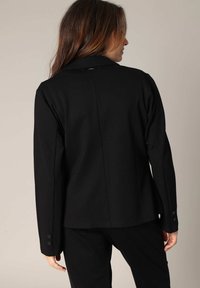 Blazer noir au design structuré, avec des manches longues, un col cranté et des accents de bouton sur les poignets. Texture de tissu lisse.