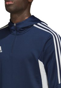 Pullover sportivo blu navy con colletto alto, chiusura con zip e strisce bianche sulle maniche. Tessuto liscio; presenta il logo del marchio sul petto.