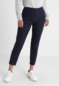 Pantalon bleu marine, fuselé avec un motif texturé et une taille élastique. Associé à des baskets blanches pour un look décontracté.