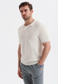 Cremefarvet kortærmet polo shirt med et struktureret mønster, flad krave og ribbede mansjetter, parret med grå stribede bukser og et ur.