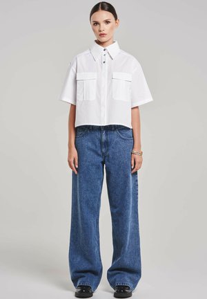 Cropped white button-up shirt with two chest pockets, paired with high-waisted, wide-leg blue denim jeans, finished with black footwear.