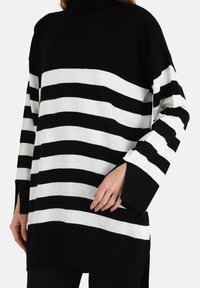 Pull rayé noir et blanc avec un col haut, une coupe ample et des manches larges. Fentes latérales notables à l'ourlet pour un confort amélioré.