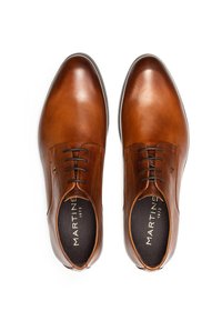 Une paire de chaussures de ville en cuir brun poli avec des lacets noirs et "MARTINE 1973" imprimé sur les semelles intérieures, présentée en vue de dessus.