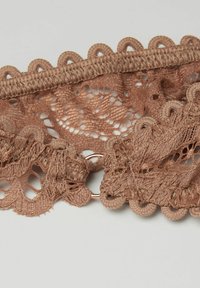 Spetsband i mjuk beige med vågiga kanter, prytt med intrikata mönster i öppen arbete och en cirkulär metallspänne. Texturerad finish.