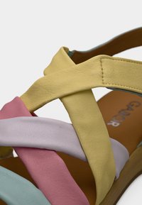 Πολύχρωμα σανδάλια με λουράκια σε κίτρινο, ροζ, λεβαντί και μέντα. Το υλικό φαίνεται υφή, με καφέ μαξιλαρέτο πάτο.