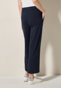 Marineblauwe wijde broek met een gestructureerde elastische tailleband en achterzakken, gecombineerd met witte sneakers met lichtblauwe accenten.