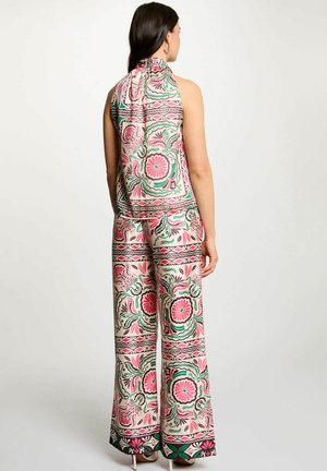 Donna che indossa un top senza maniche e pantaloni a gamba larga coordinati con motivi floreali e geometrici rosa, verdi e marroni, vista di spalle su sfondo semplice.