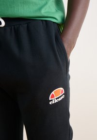 Čierne joggerské nohavice vyrobené z bavlny s elastickým pásom a bočnými vreckami. Na stehne sa nachádza farebný logo ellesse.