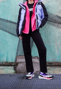 Kurtka puchowa z fioletowo-różowymi panelami, czarne akcenty; czarne spodnie; wielokolorowe sneakersy z grubą podeszwą i sznurowanym wzorem.