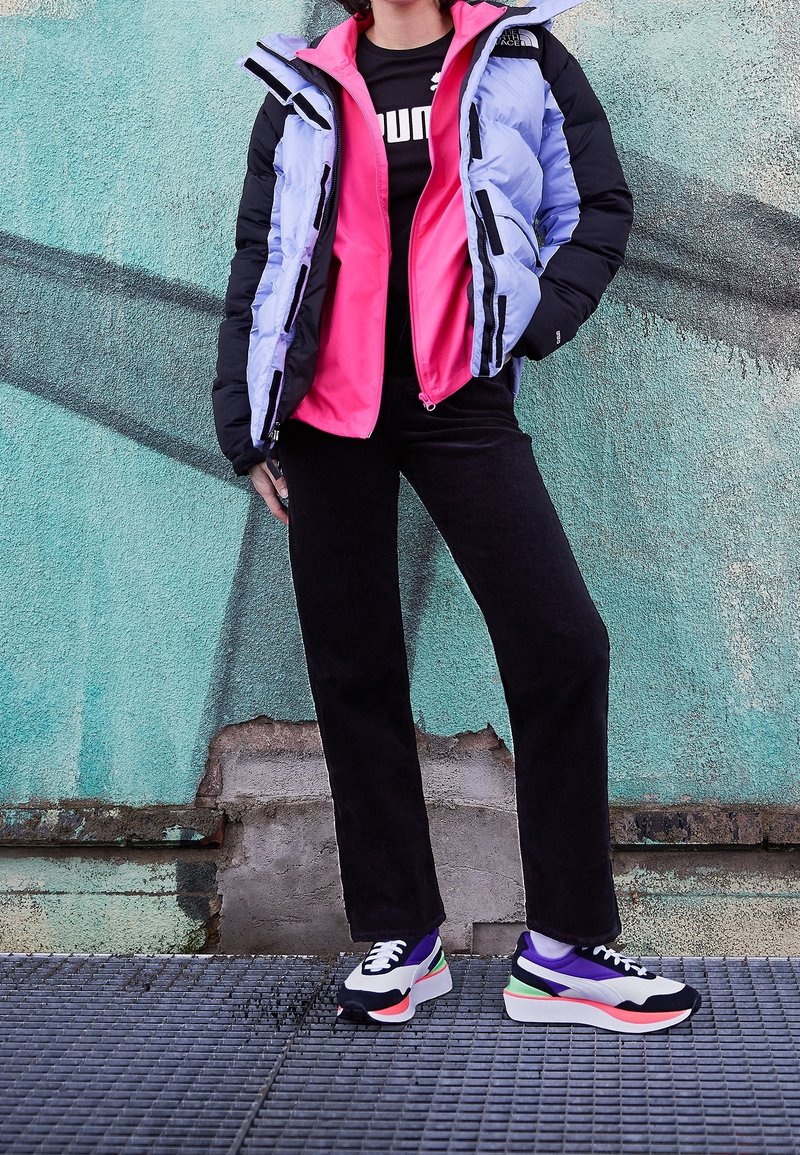 Kurtka puchowa z fioletowo-różowymi panelami, czarne akcenty; czarne spodnie; wielokolorowe sneakersy z grubą podeszwą i sznurowanym wzorem.