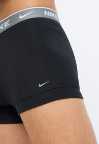Černé boxerské kraťasy Nike s šedým páskem, na kterém je bílý název značky. Hladká tkanina s těsným střihem a jemným detailem loga.