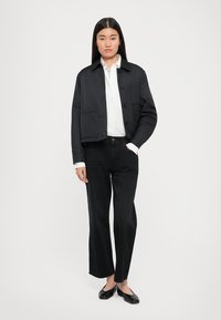 Jachetă puffer neagră, scurtă, cu închidere prin butoane, cămașă albă cu guler dedesubt, blugi negri cu picioare largi și pantofi plata negri. Textură netedă.