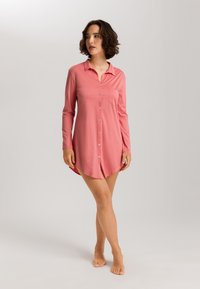 Abito camicia rosa a manica lunga in tessuto morbido, con colletto, chiusura a bottoni e tasca sul petto, dal fondo leggermente curvo.