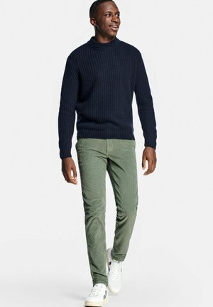 Navy ribbed knit sweater with a high collar, paired with light green corduroy pants and white sneakers. Model is walking.