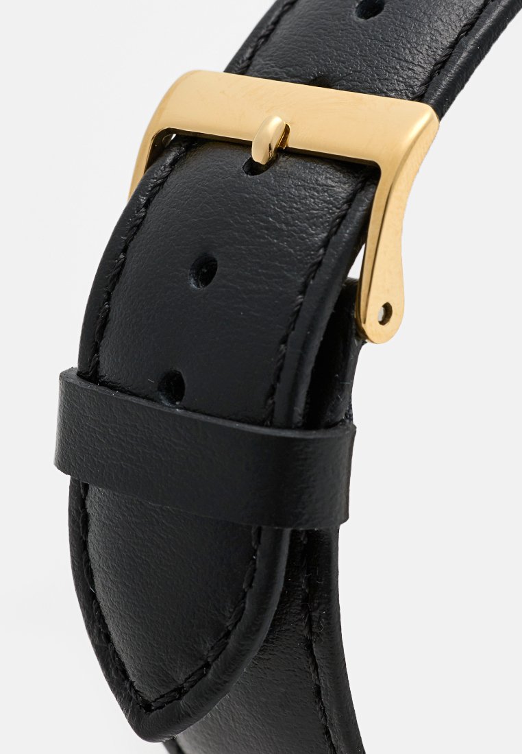 Bracciale in pelle nera con fibbia in metallo dorato. Cuciture dettagliate sui bordi e numerosi fori per la regolazione.