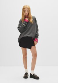 Overmaatse grijze sweatshirt met lange mouwen, gecombineerd met een zwarte rok. Accentuatie met roze boorden en gedragen met stevige zwarte loafers.