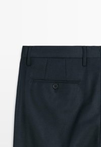 Donkerblauwe broek van een gestructureerde stof, met een enkele knop op de achterzak en een op maat gemaakte tailleband met lussen voor een riem.