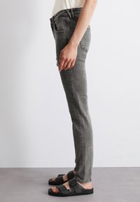Slim-fit šedé džíny vyrobené z denimu, s pěti kapsami a středním pasem. V kombinaci s černými skluznými sandály s nastavitelnými popruhy.