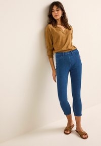 Jeans de denim azul ajustados con cintura alta, combinados con un suéter de punto suelto color beige y sandalias marrones. Textura suave, diseño limpio.
