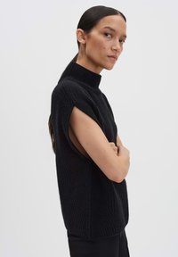 Pull en maille noire sans manches avec un col haut et des ouvertures sur les côtés, présentant une texture côtelée et une coupe décontractée.