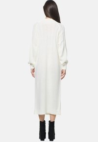 Lang, let hvid sweaterkjole med tekstureret ryg, ribbede manchetter og kant, parret med sorte platform ankelstøvler.