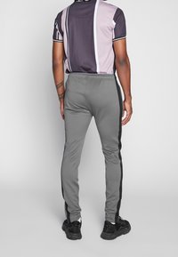 Grå sportbyxor med svarta sidremsor, elastisk midja och smal passform. Bärs med en flerfärgad t-shirt med kort ärm och svarta sneakers.