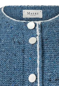 Wollene blaue Strickjacke mit strukturiertem Strickmuster, einer cremefarbenen Borte entlang der Vorderseite und drei weißen runden Knöpfen. Das Etikett trägt die Aufschrift "Maerz Muenchen."