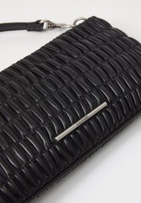 Black leather wallet featuring a textured, ribbed design. Includes a silver-colored metal accent with branding. Compact and rectangular shape.