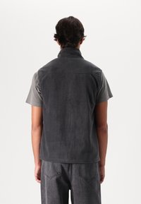Gray fleece vest with a high collar, smooth texture, and no visible fastenings, worn over a short-sleeve gray shirt.