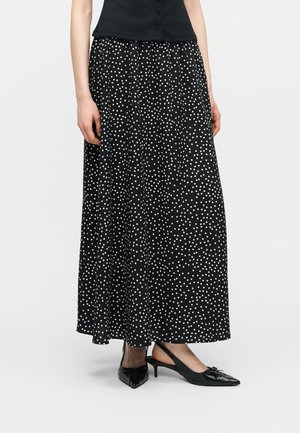 Femme portant une jupe longue noire à pois blancs, un haut noir sans manches, et des talons slingback noirs à bouts pointus avec des nœuds.