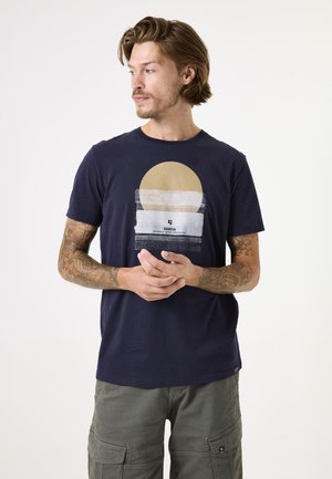 T-shirt en coton bleu marine avec un imprimé graphique d'un soleil beige et du texte. Manches courtes et col rond. Texture lisse.