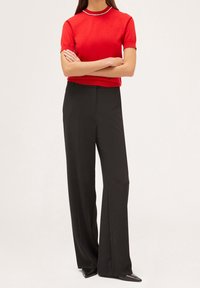 Rød kortærmet sweater med ribbestrikket halsudskæring og perlepynt, parret med højtaljede, sorte brede bukser og spidse sorte sko.