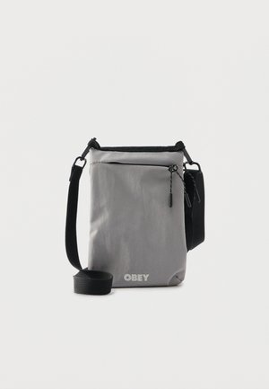 Grijze crossbodytas met een verstelbare zwarte riem, een voorvak met rits en trekkoorden, en het "OBEY"-logo onderaan in het midden.