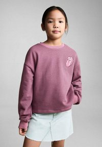 Randig rosa sweatshirt med en ribbad halsringning och ärmar; har en patch med Rolling Stones-logotypen. Bärs över en ljus denimkjol.